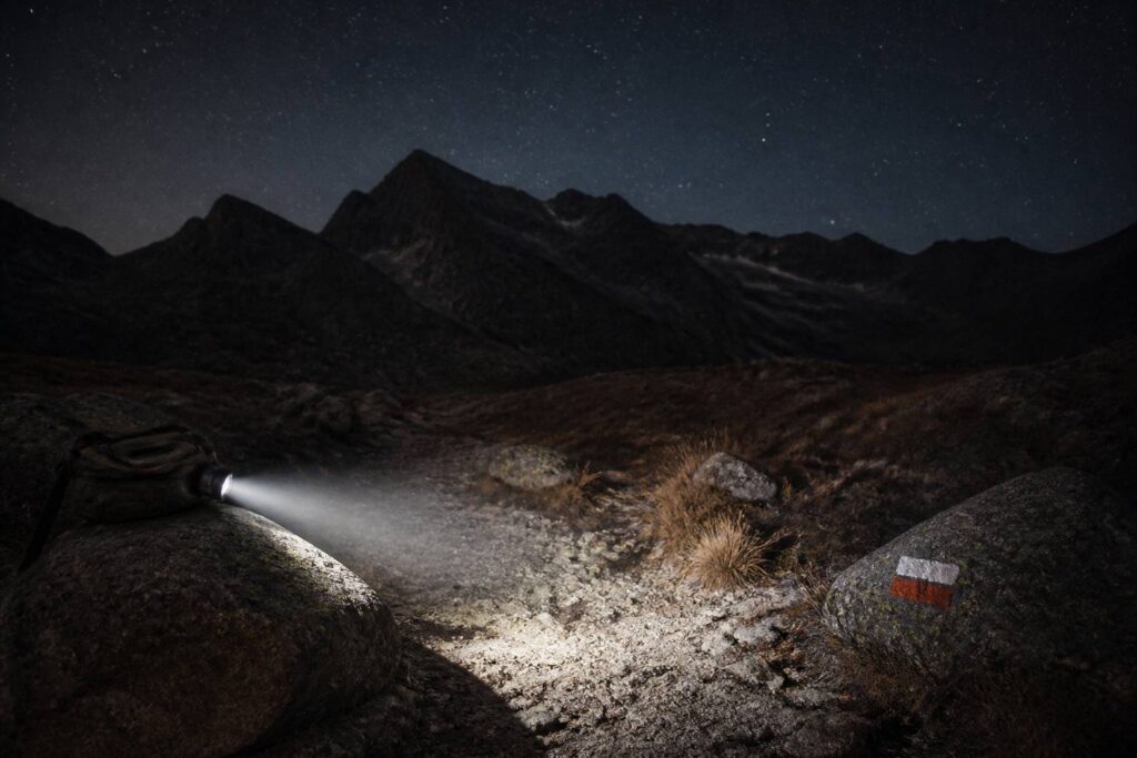 Lampe frontale allumée posée sur un sac à dos en sentier nocturne